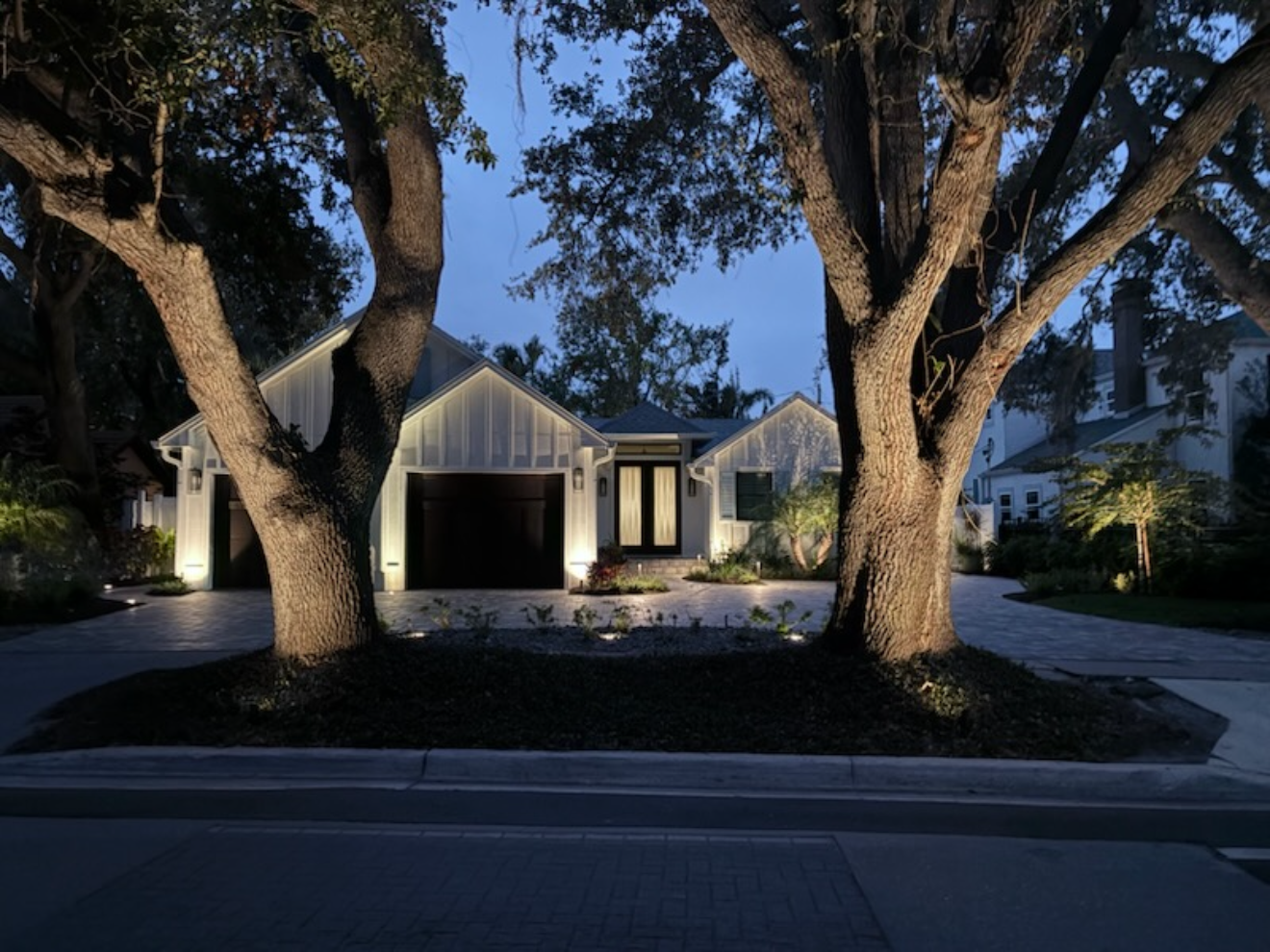 Modern home lit under oak trees at dusk